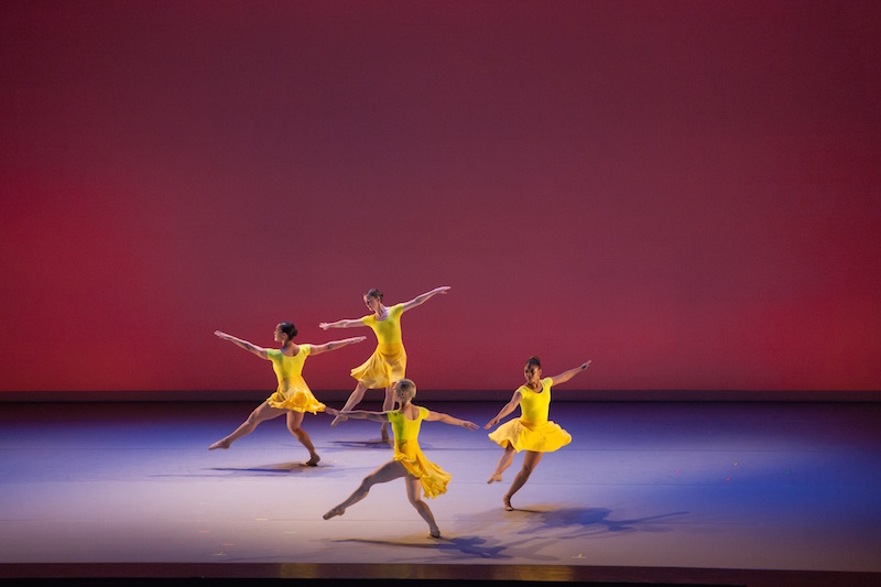 Four women in canary yellow dress with their arms outstretched as if they are ready to take flight